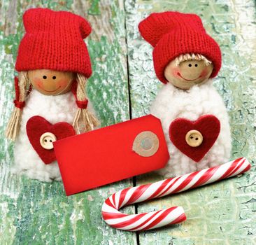 Christmas Decoration Concept with Handmade Dolls in Knit Hats, Striped Sweet Cane and Greeting Card closeup on Rustic Cracked background