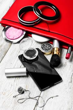 Fashionable ladies handbag with cosmetics and phone on light background