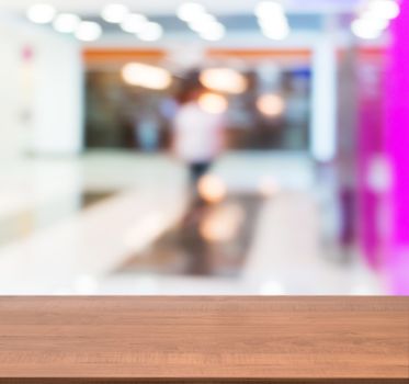 Wooden board empty table in front of blurred background. Perspective dark wood table over blur in shopping mall hall. Mock up for display or montage your product.