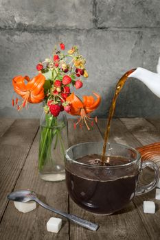 Strong tea is poured into the glass, and a bouquet with berries and lilies on the old boards