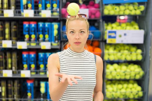 Beautiful caucasian woman shopping sports equipment in sportswear store. Lady throwing tennis ball in the air.