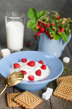 Strawberry with cream in a bowl, cookies and milk in glass on old wooden surface. Bouquet with strawberries in a vase and antique spoon in a rustic style.