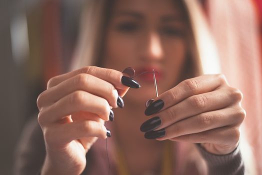 Close-up of female hands passing thread through the needle. Vintage concept.