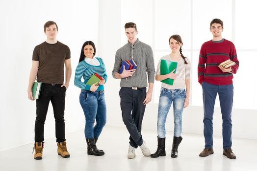 Group of cheerful students with books standing in school hall and looking at camera.