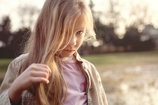 Little girl with long hair, holding a strand of hair in her hand and looking shyly at the camera.