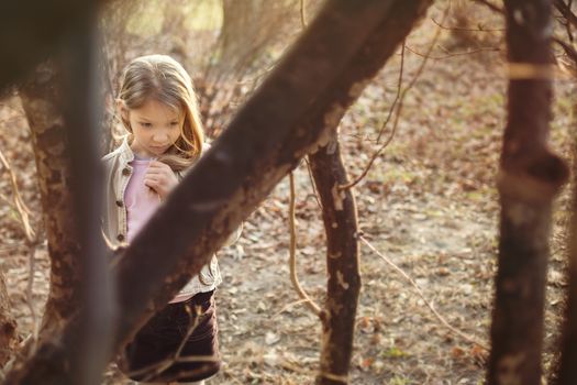 Little girl stands among the trees and with a sad expression on her face looking down.