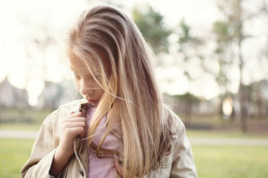 Close-up of a little girl standing alone outside with a sad expression on her face looking to the side.