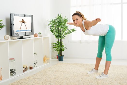 Beautiful young woman doing stretching exercises at home in front of the tv