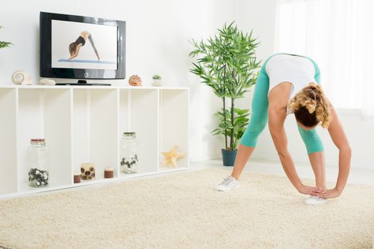 Beautiful young woman doing stretching exercises at home in front of the tv