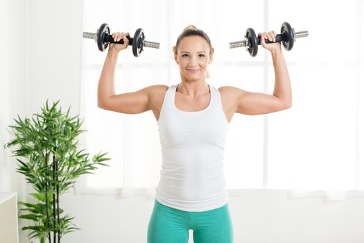 Beautiful young woman doing exercise to strengthen shoulder with dumbbells at home.