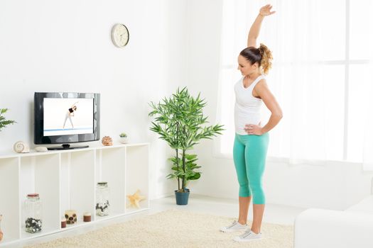 Beautiful young woman doing stretching exercises at home in front of the tv