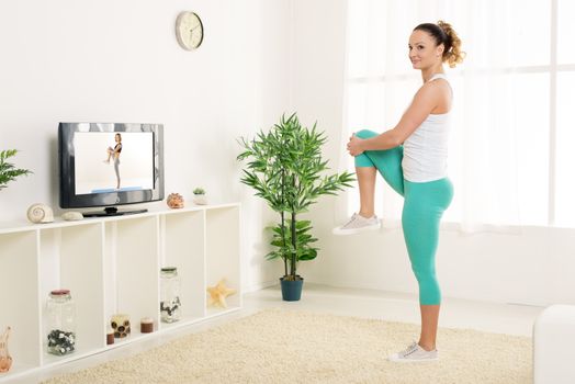 Beautiful young woman stretching out her legs at home in front of the tv