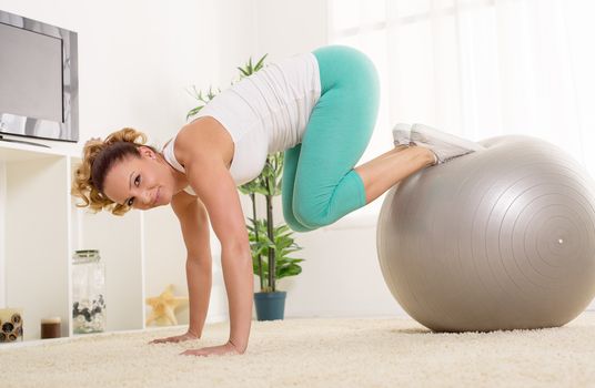 Beautiful young woman doing pilates at home in front of the tv