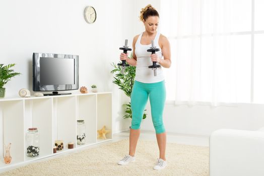 Beautiful young woman doing exercise to strengthen triceps with dumbbells at home.