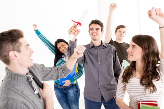 A beautiful smiling young man student with diploma. A happy group of his friends is behind him with arms raised in a fist in the air.