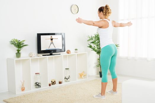 Beautiful young woman doing stretching exercises at home in front of the tv