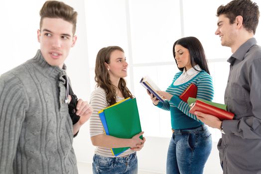 Four cheerful students with books standing in school hall and talking.