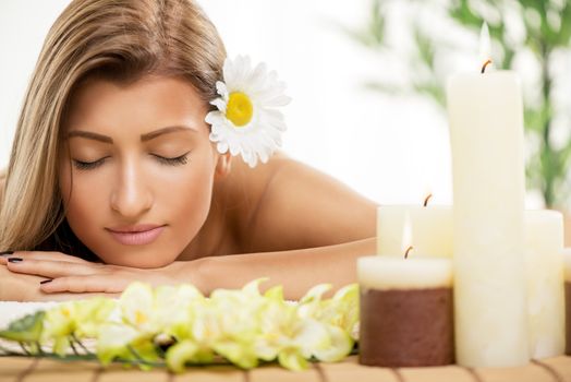 Cute young woman lying on a towel during a skincare treatment at a spa. She is relaxing  and enjoying with eyes closed. 