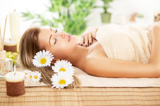 Cute young woman lying on a towel during a skincare treatment at a spa. She is enjoying with eyes closed.
