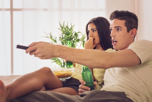 Beautiful couple sitting at home and watching horror movie.