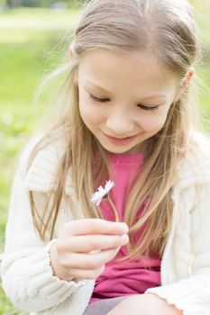 Smiling cute little girl in the park holding white flower and looking at him.