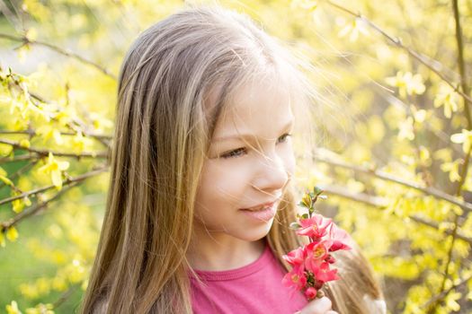 Smiling little girl smelling spring flower in the park and looking to the side.