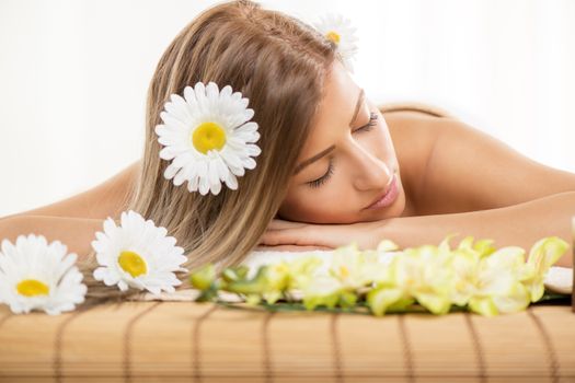 Cute young woman lying on a towel during a skincare treatment at a spa. She is relaxing  and enjoying with eyes closed. 