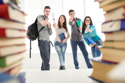 A beautiful smiling young student girl with diploma is standing with happy group of his friends with arms raised in a fist in the air.