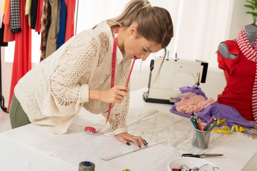 Young woman, fashion designer, with tape measure draped over the neck, drawing with a ruler on sewing pattern.