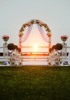 Wedding ceremony by the river at sunset. Arch decorated with flowers in the center of the composition