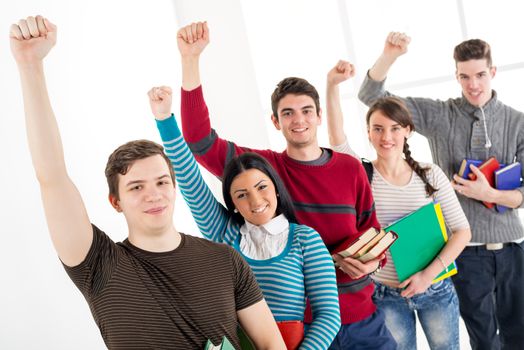 Group of cheerful students with book's standing In A Row with arms raised in a fist in school hall and looking at camera.