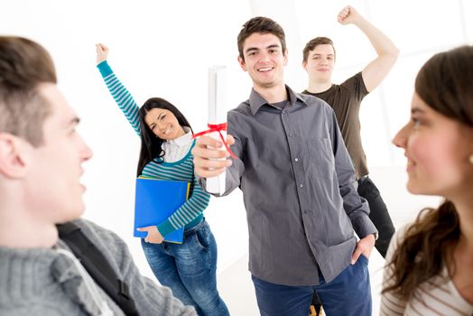 A beautiful smiling young man student with diploma. A happy group of his friends is behind him with arms raised in a fist in the air.