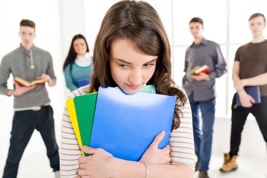 A beautiful thinking girl with book's is standing in the foreground. A group of her friends is behind her. 