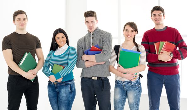 Group of cheerful students with book's standing in school hall and looking at camera.