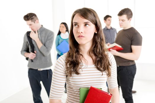 A beautiful thinking girl with book's is standing in the foreground. A group of her friends is behind her. 