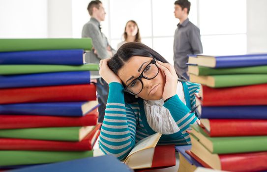 Portrait of tired student girl with glasses sitting and learning among the many book's in the foreground. 