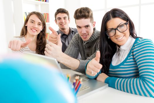 Group of cheerful students learning. They sitting with thumb up and looking at camera.