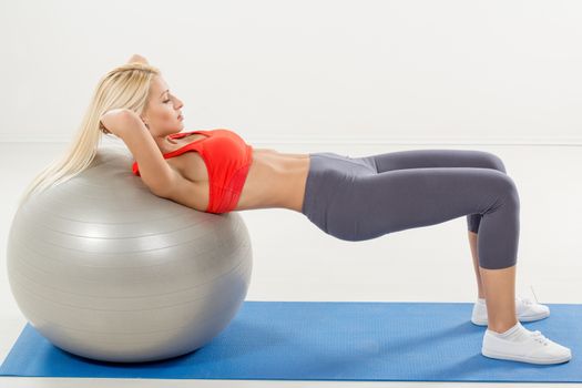 Cute young woman exercising sit-ups supported on a fitness ball 