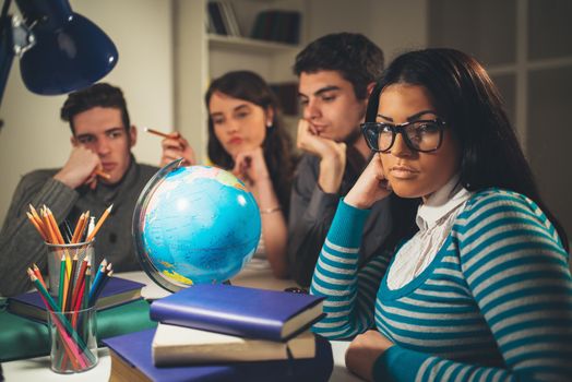 A beautiful girl students of Geography sitting and looking at camera in the foreground. A Group of her friends is behind learning with globe and thinking. Vintage concept.