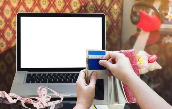 Hands pull credit or debit card out of wallet with laptop or computer notebook background, women shopping online via internet with measure tape and blank screen notebook background