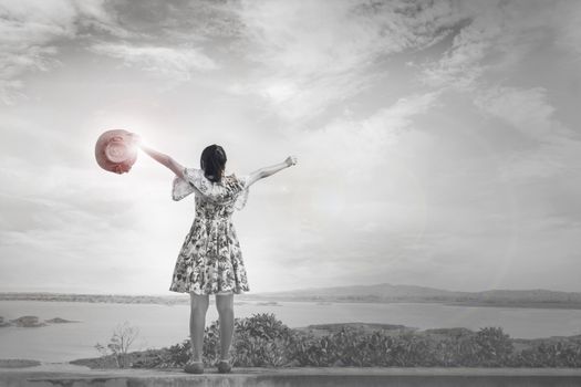 Black and white picture of back or rare view girl or women standing and raising arms up high to sky embrace world freely with lens flare light on reservoir or lake background, girl in relax and freedom mood in light of hope