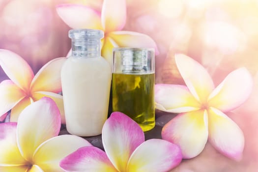 Mini set of bubble bath and shower gel liquid with pink flowers plumeria or frangipani on timber or log wooden background,shampoo and conditioner spa treatment in dreamy sweet bokeh