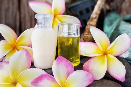 Mini set of bubble bath and shower gel liquid with pink flowers plumeria or frangipani on timber or log wooden background,shampoo and conditioner spa treatment