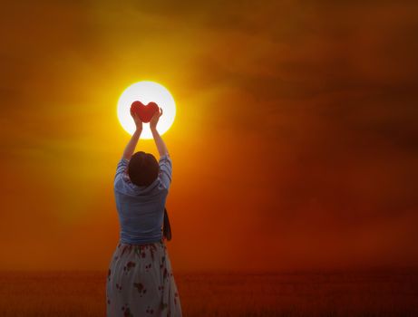 Back or rare view of women gently hold red heart with love, care and restpect to the sun on grass field and sunset twilight background