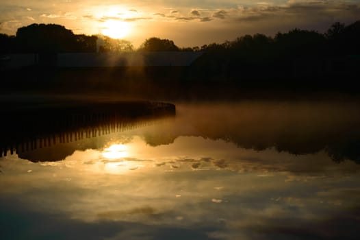 Beautiful sunset reflection over a tranquil freshwater lake with the fiery orb of the sun and scattered clouds mirrored on the surface of the calm water at dusk