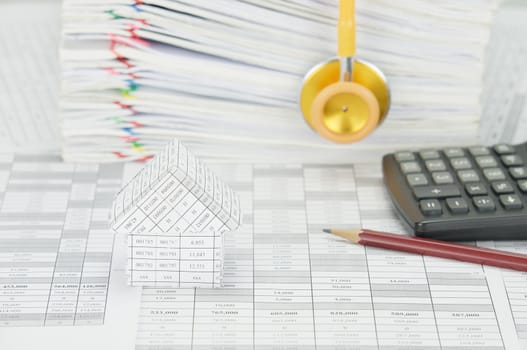 House on finance account have blur yellow and gold stethoscope with pile paperwork of report with colorful paperclip and pencil with calculator as background.