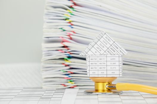 House on yellow and gold stethoscope on finance account have blur pile paperwork of report with colorful paperclip as background.