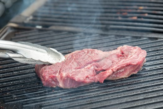 the raw steak with spices on metal grill