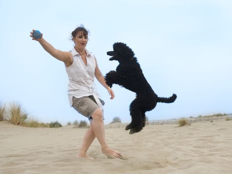 woman playing with poodle on the beach