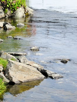 Bank of the river with stones on blue sky background